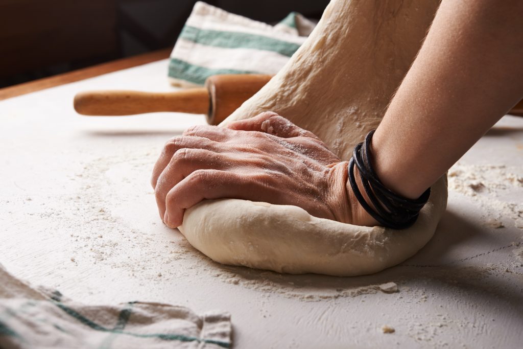 mains qui pétrissent de la pâte sur plan de travail fariné près d'un rouleau à pâtisserie