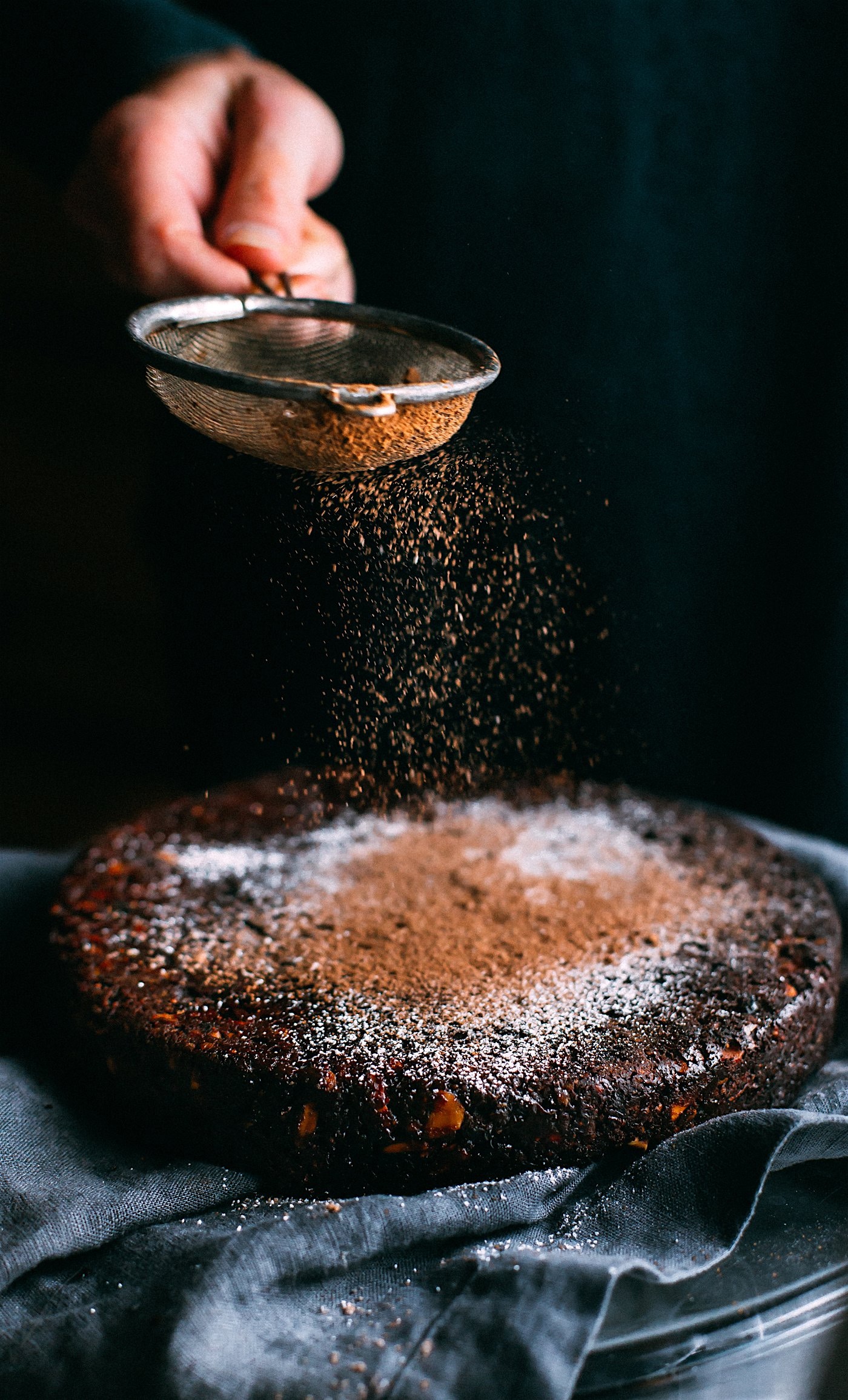 personne saupoudrant du chocolat en poudre sur un gâteau au chocolat